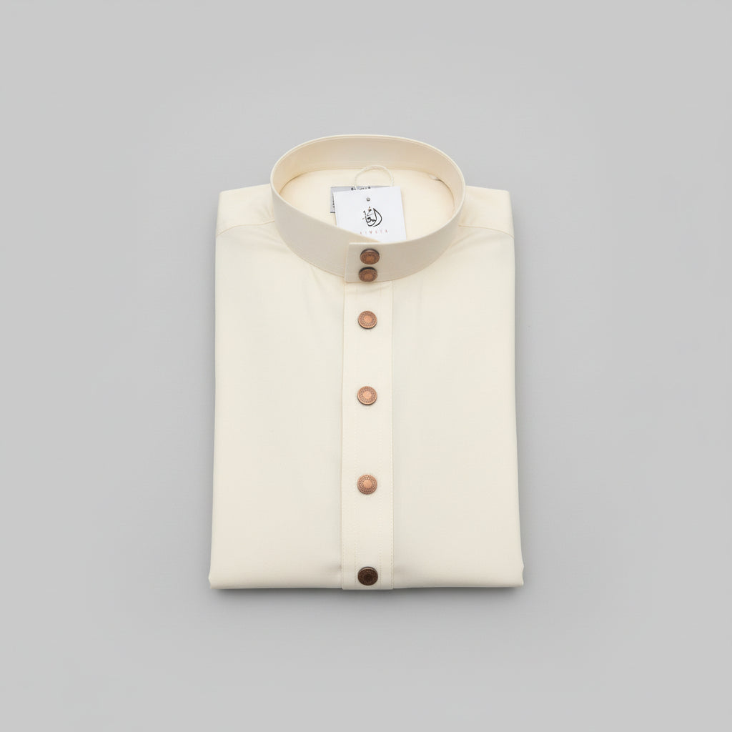 A folded cream-colored thobe with a stand-up collar and a vertical button placket, placed on a wooden surface. A white brand tag is attached near the collar.