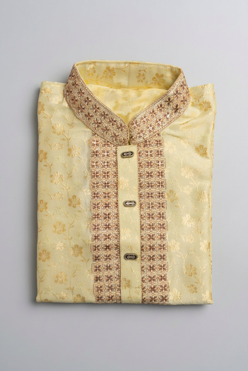 A folded light yellow kurta with gold floral patterns and brown embroidered trim on the collar, placket, and front buttons, displayed on a dark textured background.