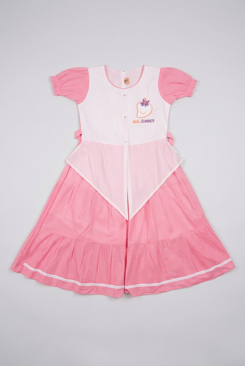 A pink and white children's dress laid flat on a piece of cardboard on a gray tiled floor. The dress has a white bodice with pink sleeves and a pink pleated skirt with white piping.