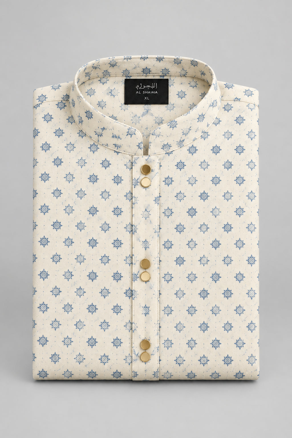 A folded cream-colored shirt with a light blue star pattern, featuring a button-down front and a black size tag, laid flat on a gray surface.
