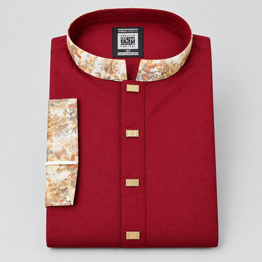 A folded red traditional men's shirt with a patterned collar and sleeve cuff, gold-tone buttons, and a hanging brand tag on a dark blue surface.