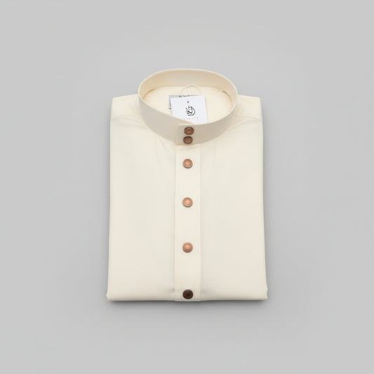 A folded cream-colored thobe with a stand-up collar and a vertical button placket, placed on a wooden surface. A white brand tag is attached near the collar.
