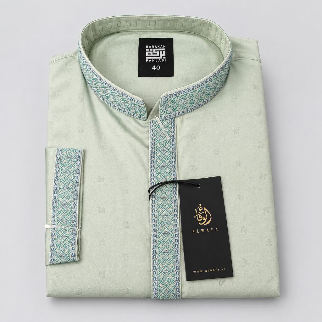A folded light green traditional long-sleeve shirt with a mandarin collar and patterned trim, displayed on a dark blue fabric surface with a black Alwaia brand tag attached.