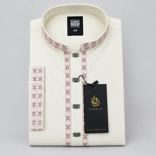 An off-white/cream men's kurta laid flat on a dark blue fabric surface, featuring a patterned pink and beige mandarin collar and front placket, a matching patterned belt, and a black hangtag with gold branding.