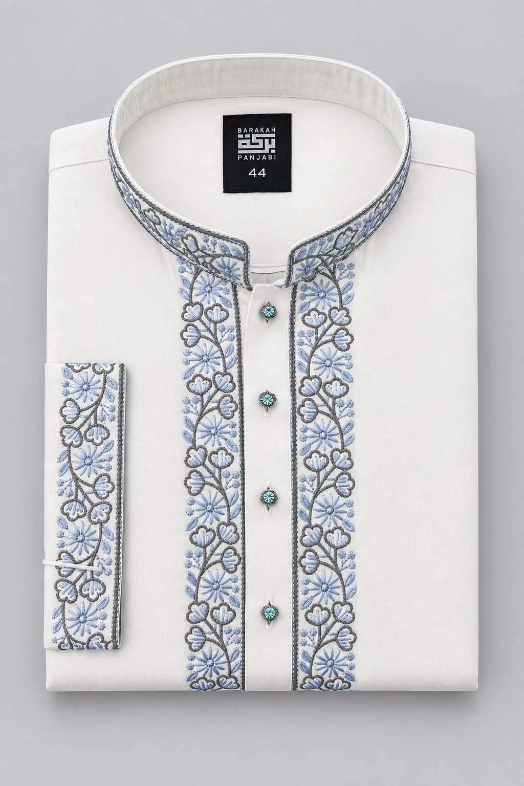 A folded white kurta shirt with blue and gray floral embroidery on the collar, placket, and sleeve, featuring decorative turquoise-colored buttons. The brand label 'Bharat SSP Fabrics' is visible inside the collar.