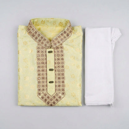 A folded light yellow embroidered kurta with a patterned neckline and a white folded matching fabric piece, laid flat on a dark gray textured surface.