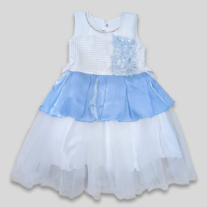 A sleeveless girls' party dress with a white textured bodice, a light blue ruffled overlay, and a layered white tulle skirt, laid flat on a cardboard background.