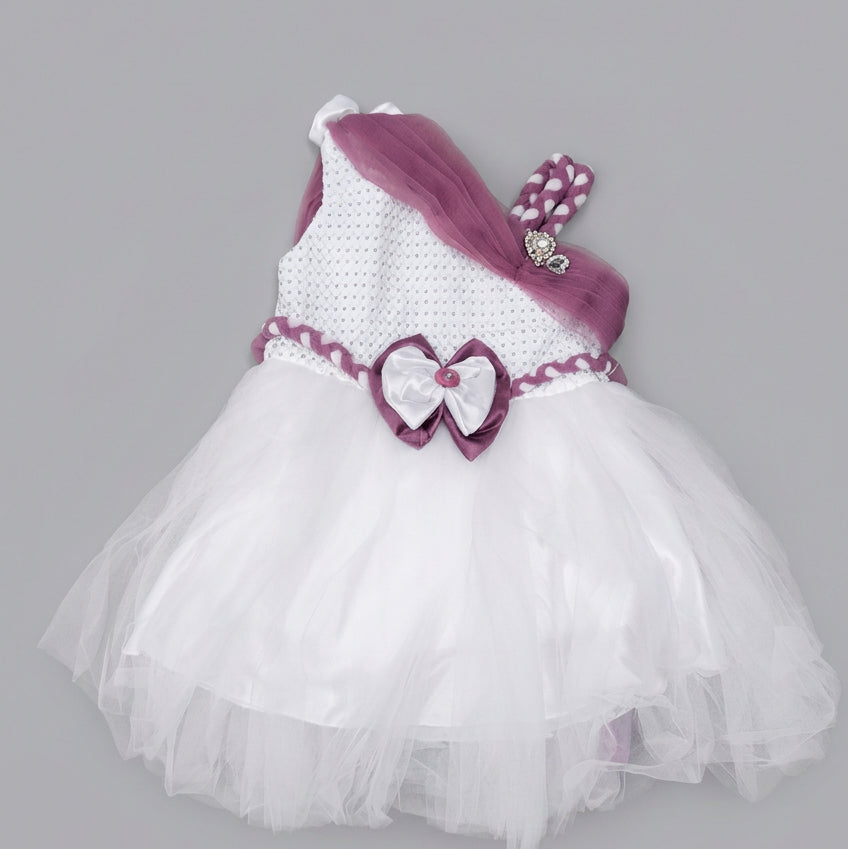 A toddler girl's one-shoulder tutu dress in white and purple, featuring a textured knit bodice, a white tulle skirt, a purple sash, and a heart-shaped bow at the waist.