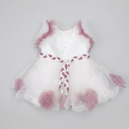 A white tutu dress with dusty purple ruffle accents and a matching braided headband, laid flat on a brown cardboard background.