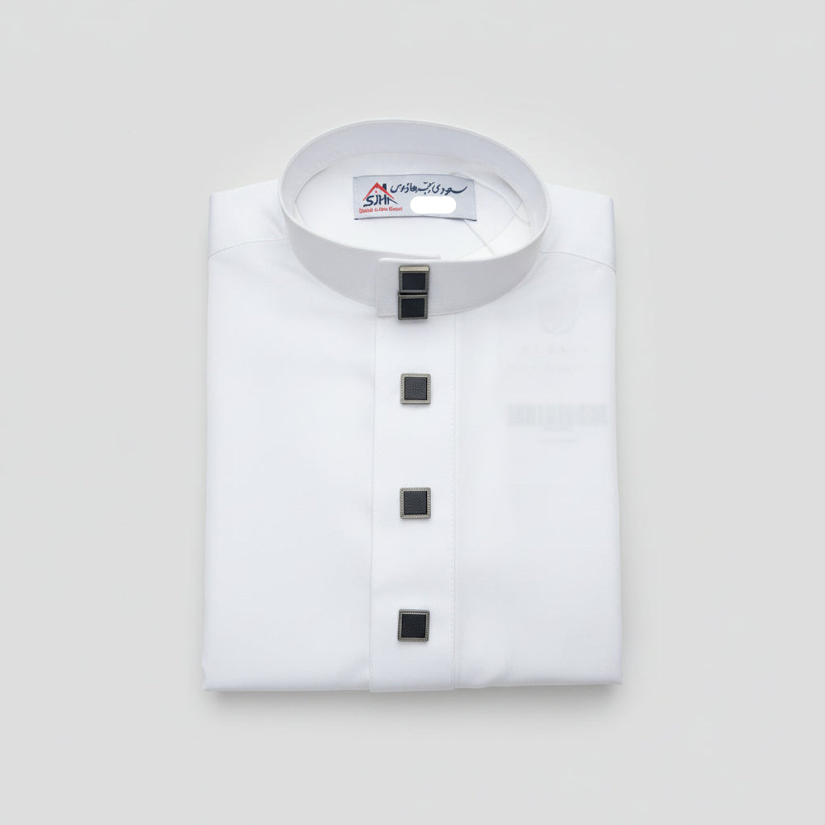 A folded white long-sleeve collared thobe with a stand collar and four black square buttons down the front, placed on a gray surface.
