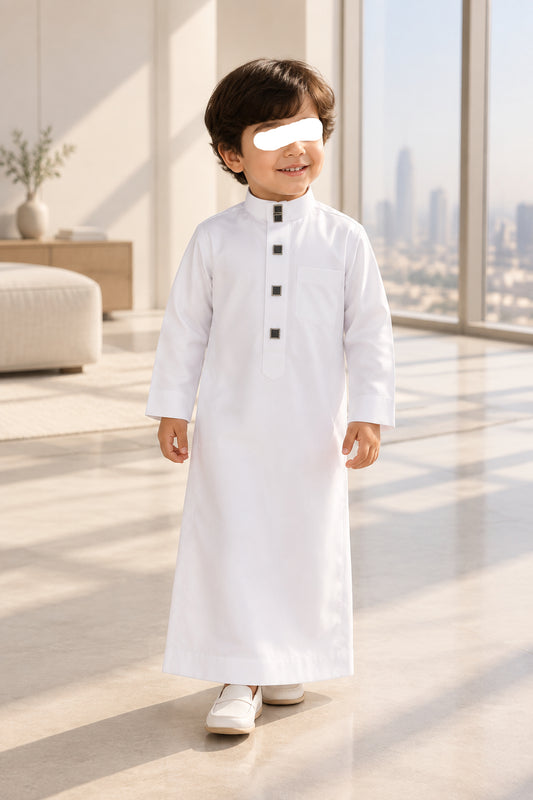 A folded white long-sleeve collared thobe with a stand collar and four black square buttons down the front, placed on a gray surface.